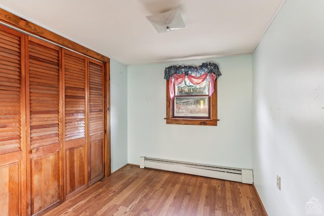 unfurnished bedroom featuring a closet, a baseboard radiator, and hardwood / wood-style flooring