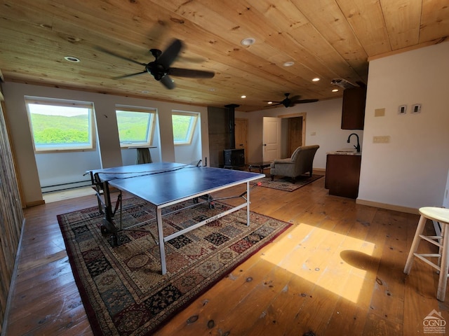 recreation room with light hardwood / wood-style floors, a wood stove, a wealth of natural light, and wood ceiling