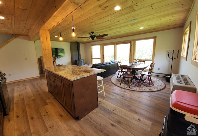 kitchen featuring light stone counters, pendant lighting, light hardwood / wood-style flooring, wooden ceiling, and a wood stove