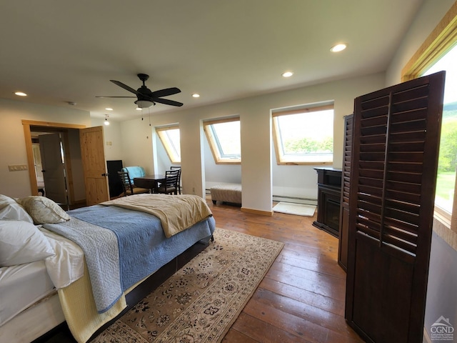 bedroom with a skylight, ceiling fan, a baseboard heating unit, hardwood / wood-style flooring, and a fireplace