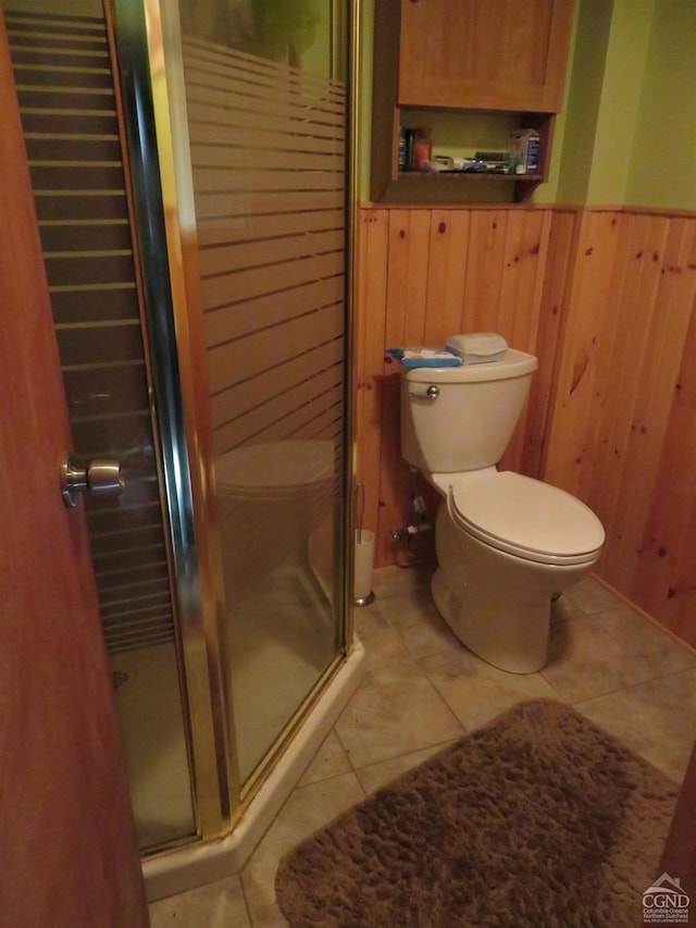 bathroom with tile patterned flooring, toilet, an enclosed shower, and wooden walls