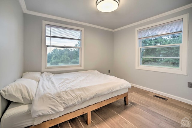 bedroom with multiple windows, ornamental molding, and hardwood / wood-style flooring