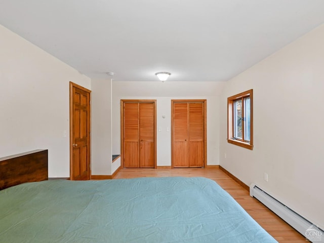 unfurnished bedroom featuring two closets, light wood-type flooring, and a baseboard radiator