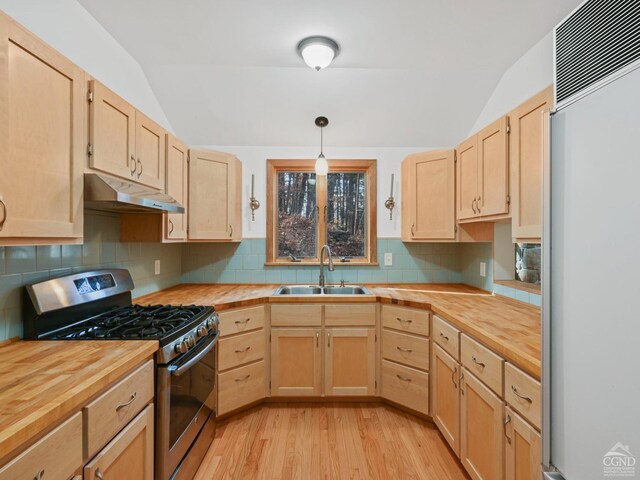 kitchen featuring paneled refrigerator, vaulted ceiling, sink, pendant lighting, and stainless steel gas stove