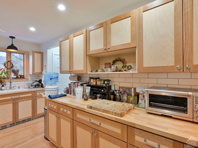 kitchen featuring wooden counters, sink, light brown cabinetry, decorative light fixtures, and light hardwood / wood-style floors