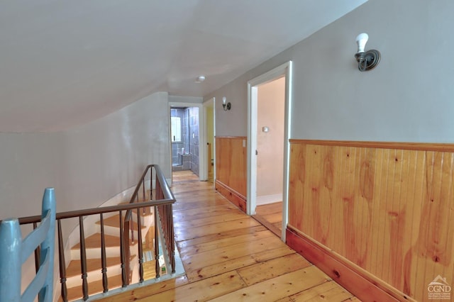 hall with lofted ceiling, wooden walls, and light hardwood / wood-style flooring