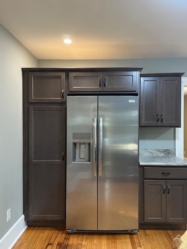 kitchen featuring light stone countertops, stainless steel fridge, and light wood-type flooring