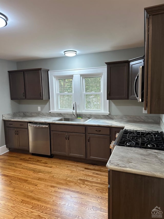 kitchen with dark brown cabinetry, sink, appliances with stainless steel finishes, and light hardwood / wood-style flooring