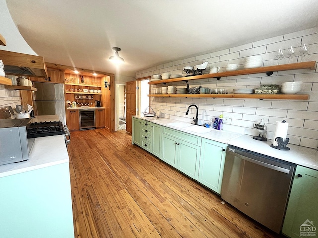 kitchen with sink, stainless steel appliances, wine cooler, light hardwood / wood-style floors, and green cabinetry