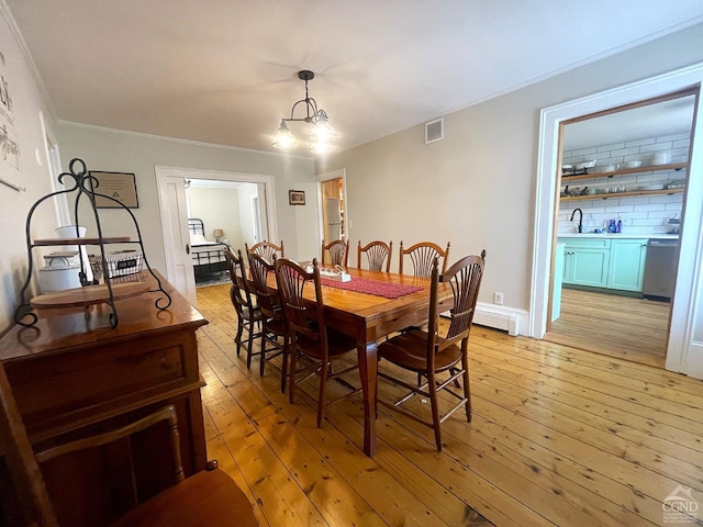 dining space with crown molding, sink, light hardwood / wood-style floors, and a notable chandelier