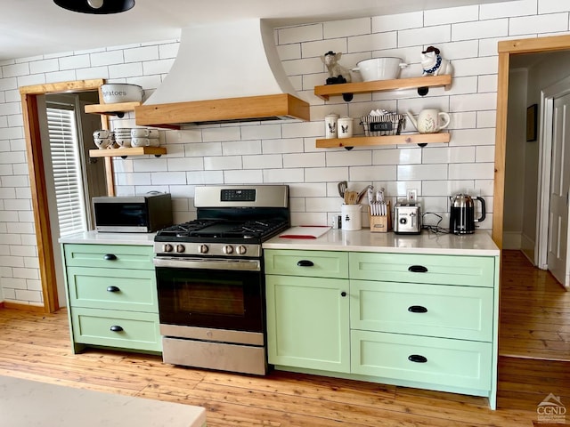 kitchen with stainless steel appliances, premium range hood, light wood-type flooring, decorative backsplash, and green cabinetry