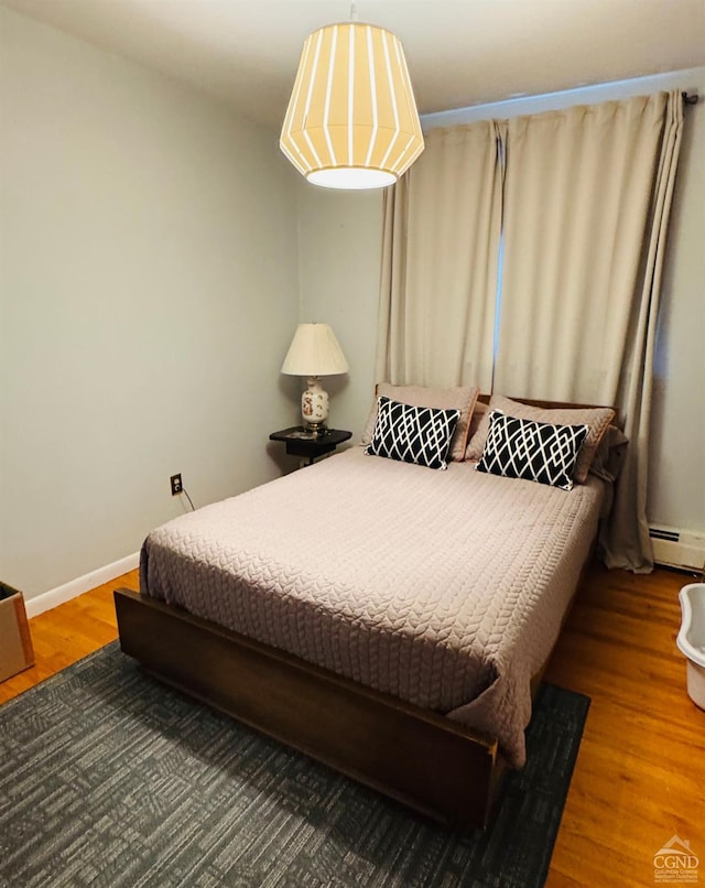 bedroom with hardwood / wood-style floors and a baseboard heating unit