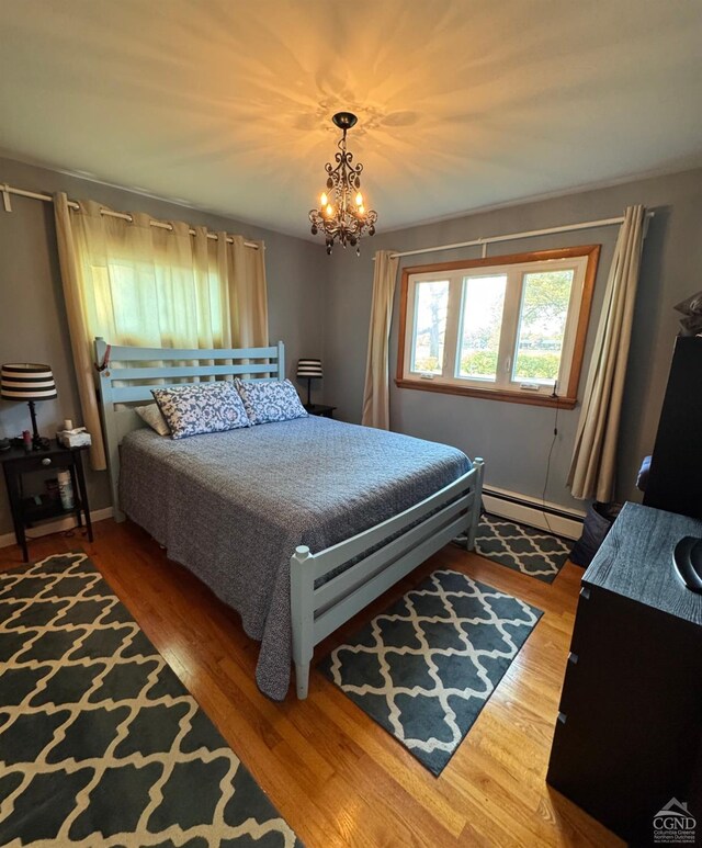 bedroom featuring baseboard heating, a notable chandelier, and hardwood / wood-style flooring