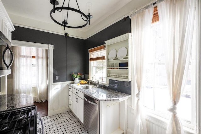 kitchen with stainless steel appliances, a sink, white cabinets, wainscoting, and crown molding