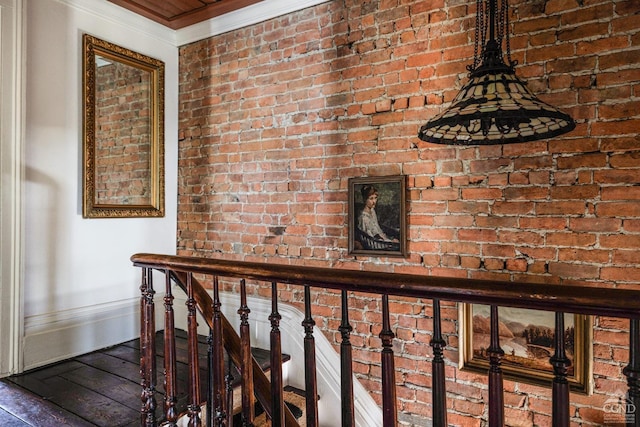 hall with ornamental molding, brick wall, hardwood / wood-style floors, and an upstairs landing