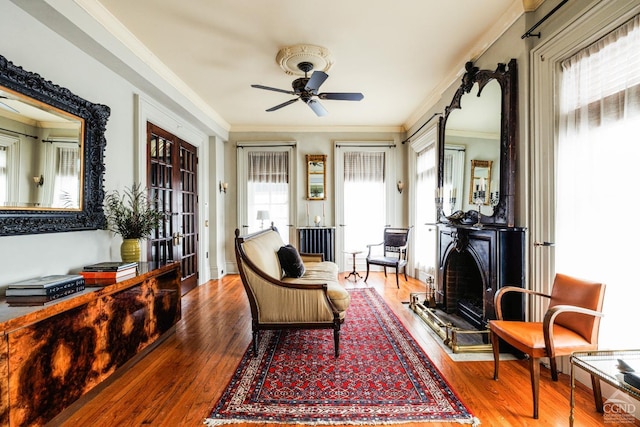 living area with wood finished floors, a ceiling fan, and crown molding