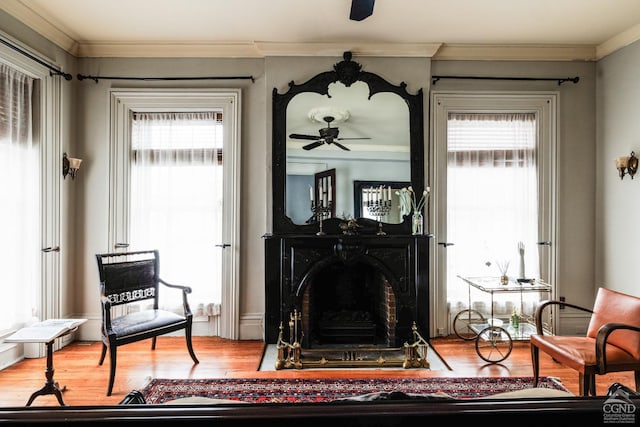 living area with a fireplace with flush hearth, ceiling fan, wood finished floors, and crown molding