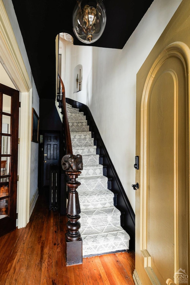 stairway with arched walkways, wood finished floors, and baseboards