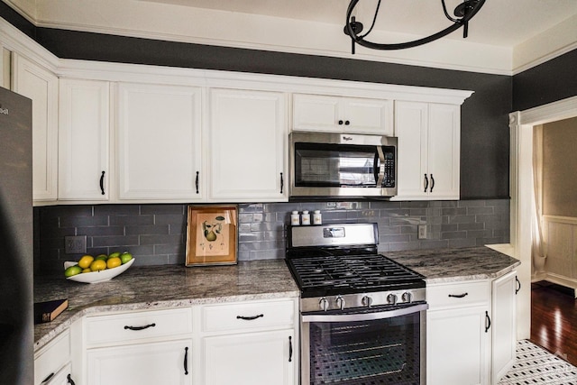 kitchen with stone countertops, stainless steel appliances, wood finished floors, white cabinetry, and backsplash