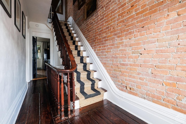 stairs featuring brick wall and hardwood / wood-style floors