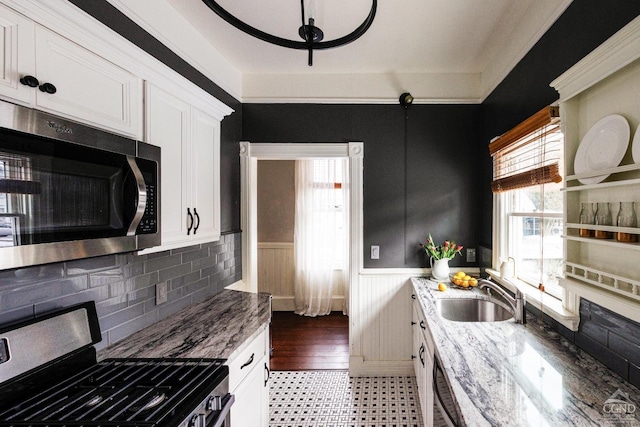 kitchen with light stone counters, appliances with stainless steel finishes, white cabinets, wainscoting, and a sink