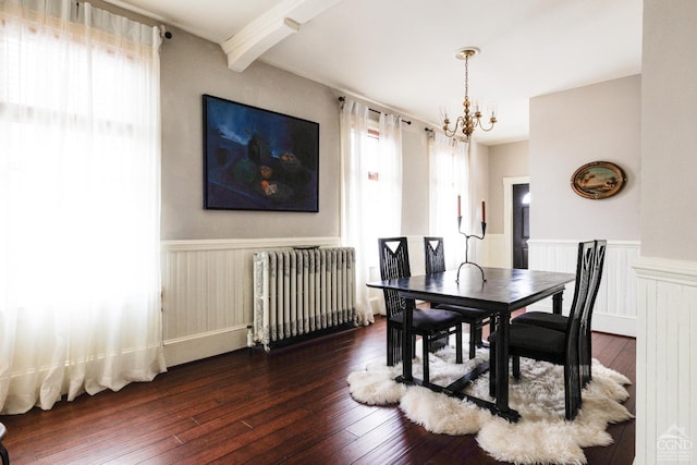 dining room with dark wood-type flooring, a chandelier, a wainscoted wall, and radiator heating unit