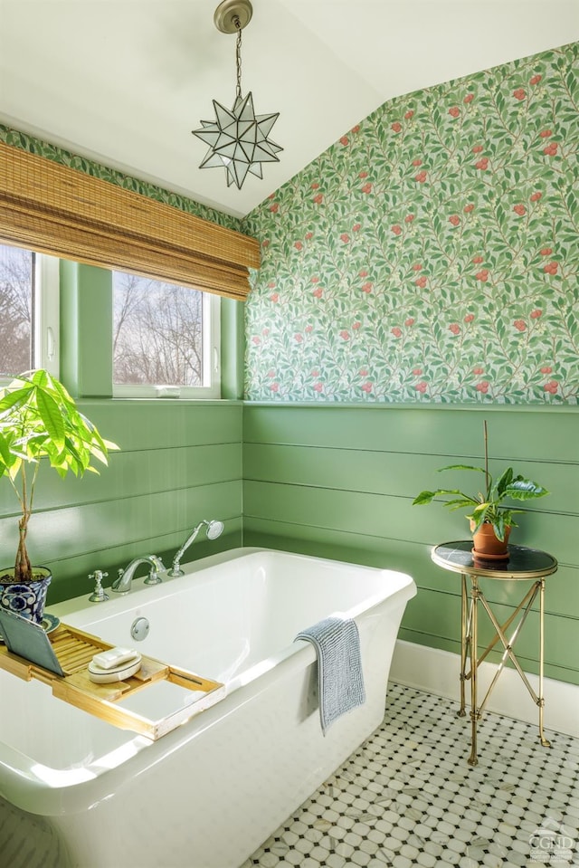 bathroom featuring lofted ceiling, wainscoting, a freestanding bath, and wallpapered walls