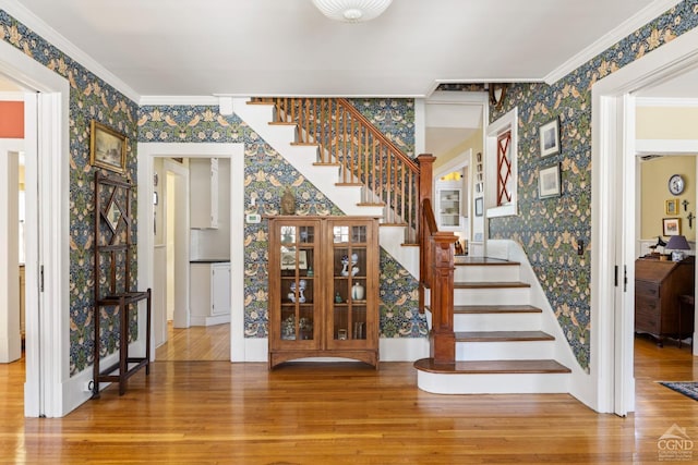 staircase featuring wallpapered walls, ornamental molding, and wood finished floors