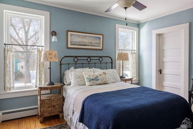 bedroom featuring ceiling fan, a baseboard heating unit, crown molding, and wood finished floors