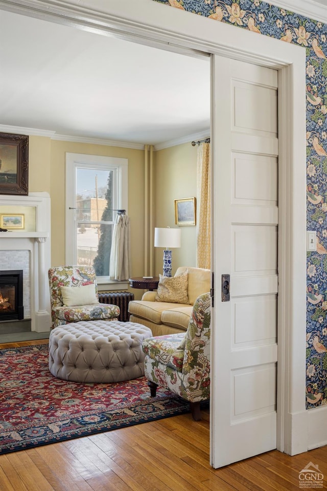 living area with crown molding, a lit fireplace, and wood finished floors