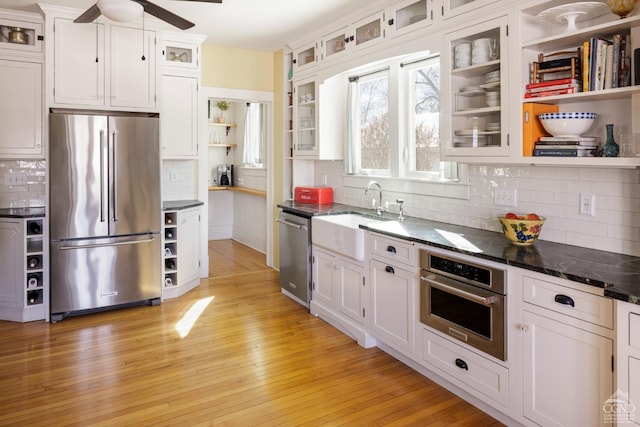 kitchen with stainless steel appliances, a sink, white cabinetry, open shelves, and glass insert cabinets