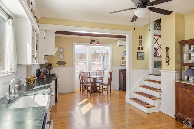 kitchen featuring a sink, white cabinetry, a wall mounted AC, wainscoting, and dark countertops