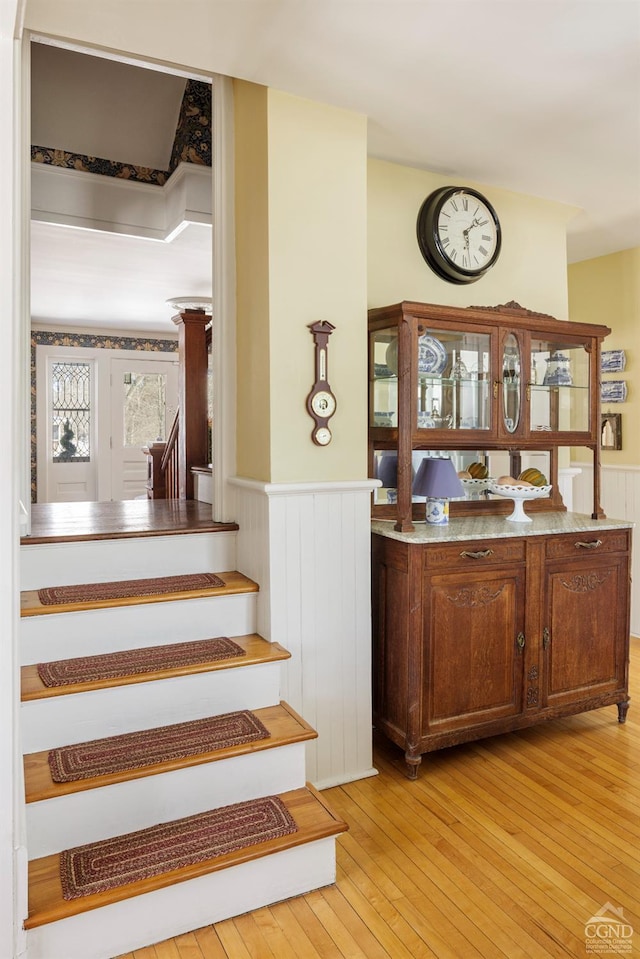 bar featuring a wainscoted wall, stairs, and light wood finished floors