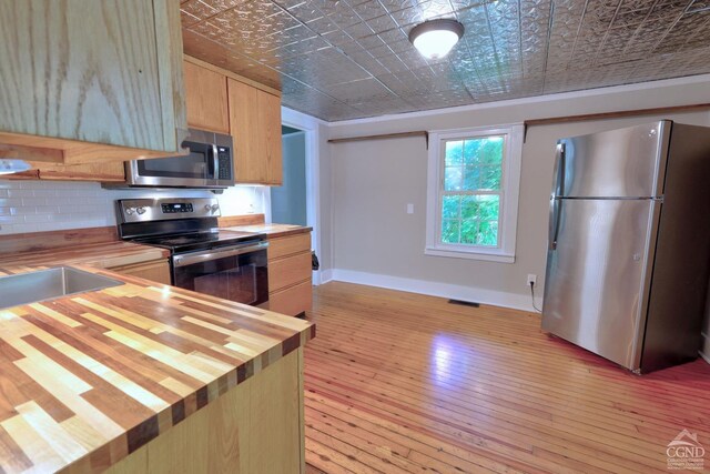 kitchen featuring wooden counters, appliances with stainless steel finishes, light brown cabinetry, sink, and light hardwood / wood-style floors