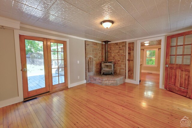 unfurnished living room with light hardwood / wood-style floors, a wood stove, and ornamental molding