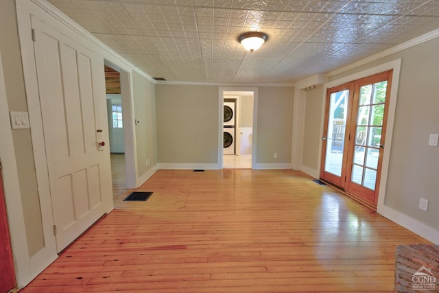 unfurnished room featuring french doors, ornamental molding, stacked washer / drying machine, and light wood-type flooring