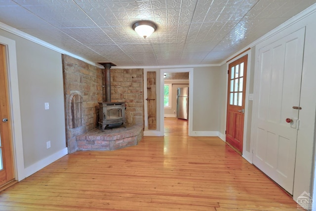 unfurnished living room featuring light wood-type flooring, a wood stove, and ornamental molding