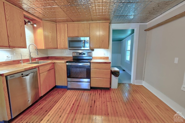 kitchen with decorative backsplash, appliances with stainless steel finishes, wood counters, sink, and light hardwood / wood-style floors