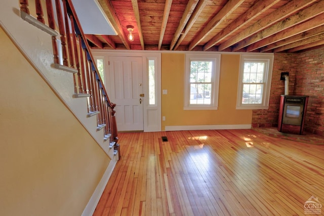 foyer entrance featuring brick wall, light hardwood / wood-style flooring, wooden ceiling, beamed ceiling, and a wood stove