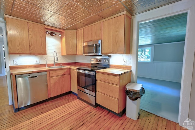 kitchen with appliances with stainless steel finishes, light hardwood / wood-style flooring, butcher block counters, and sink