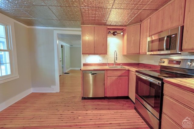 kitchen with sink, stainless steel appliances, wood counters, light hardwood / wood-style flooring, and backsplash