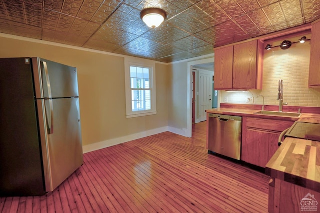 kitchen featuring appliances with stainless steel finishes, ornamental molding, light hardwood / wood-style floors, sink, and butcher block countertops