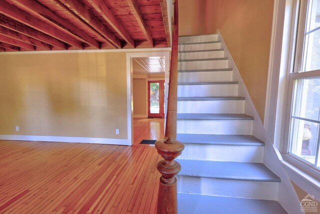 staircase featuring beamed ceiling, wood ceiling, and hardwood / wood-style flooring