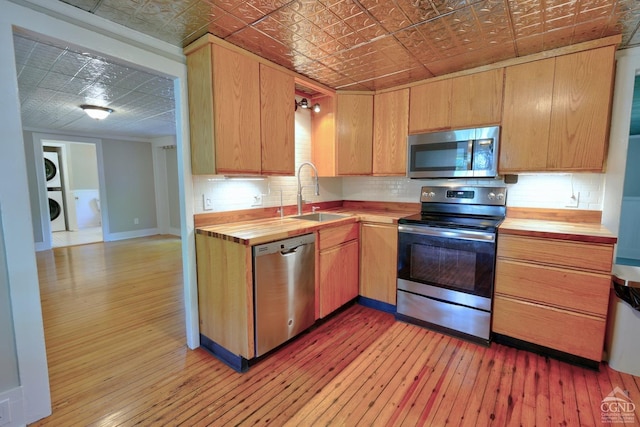 kitchen with appliances with stainless steel finishes, light wood-type flooring, stacked washer and clothes dryer, and sink