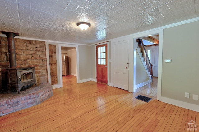 entryway with a textured ceiling, light hardwood / wood-style floors, a wood stove, and ornamental molding