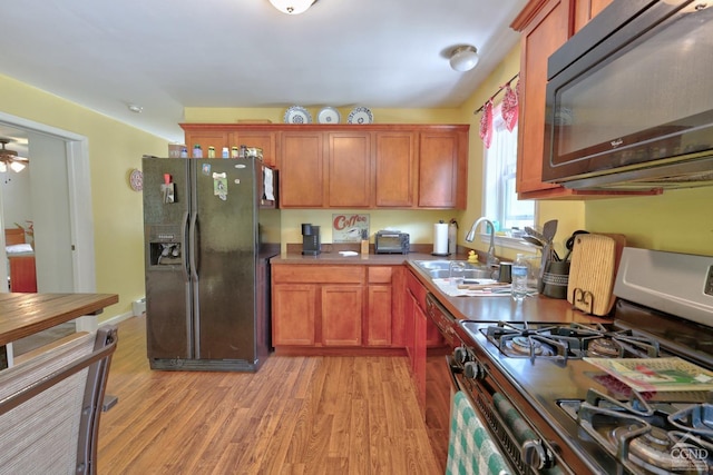 kitchen with black appliances, ceiling fan, light wood-type flooring, and sink