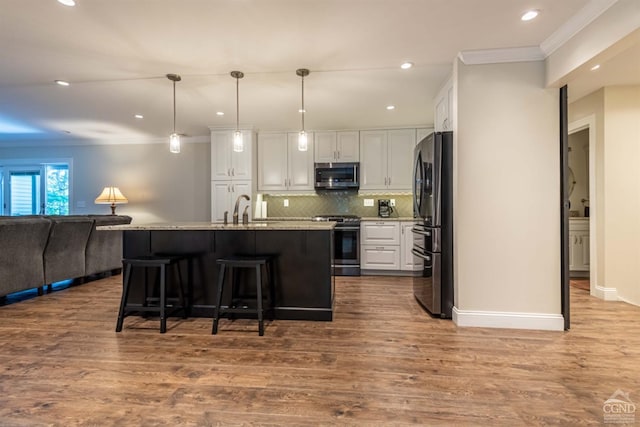 kitchen with a center island with sink, appliances with stainless steel finishes, sink, white cabinetry, and decorative light fixtures