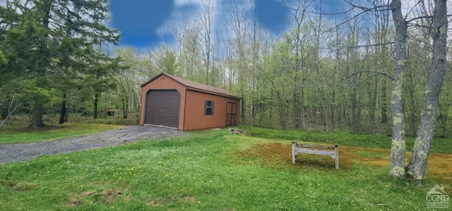 view of yard featuring a garage, driveway, an outbuilding, and a wooded view