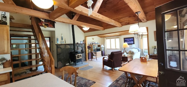 living area featuring lofted ceiling with beams, a wood stove, stairs, and wood finished floors