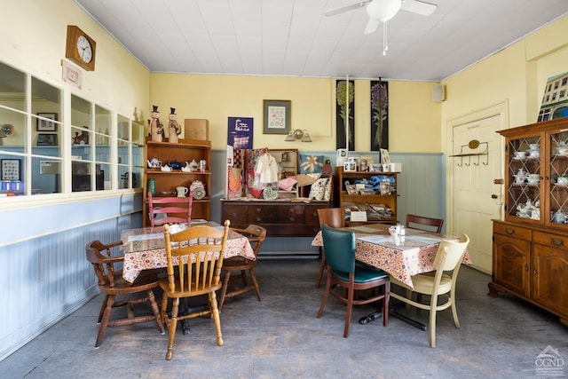 dining room with ceiling fan, wooden walls, and concrete floors